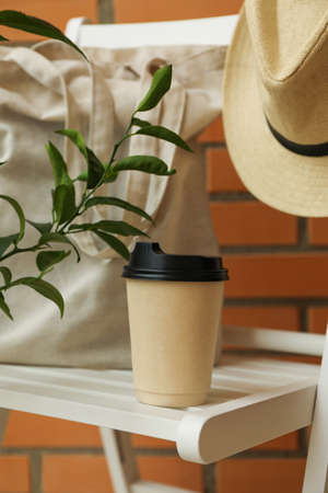 Wooden chair with hat, paper cup and cotton bag against brick wall backgroundの写真素材