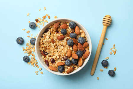 Bowl with granola and dipper on blue background