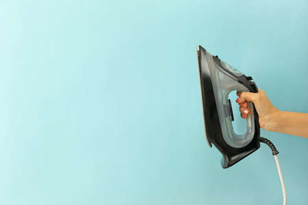 Female hand hold modern iron on blue backgroundの写真素材