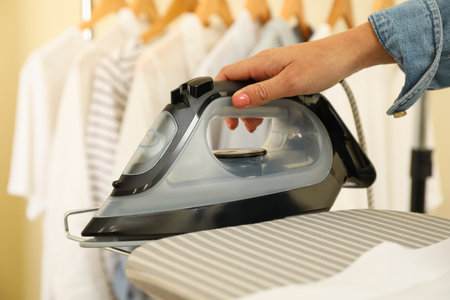 Female hand hold modern iron on ironing board, close upの写真素材