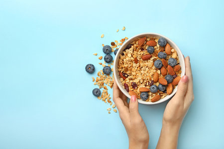 Female hands hold bowl with granola on blue backgroundの写真素材