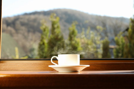 Saucer with cup of hot drink on wooden windowsillの写真素材