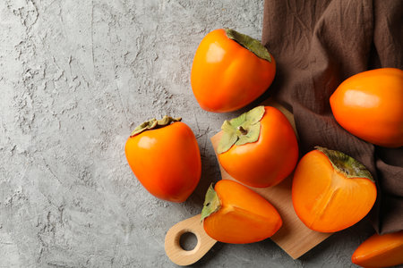Board with ripe persimmon and kitchen towel on gray backgroundの写真素材