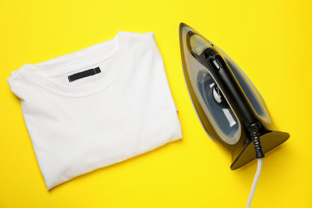 Modern iron and folded t-shirt on yellow background, top viewの写真素材