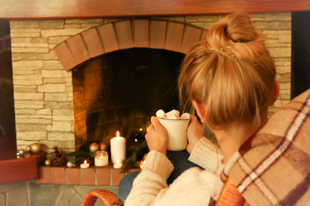 Woman sitting with cup of marshmallows near the Christmas fireplaceの写真素材