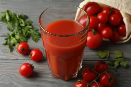 Glass of tomato juice and tomatoes on gray wooden tableの写真素材