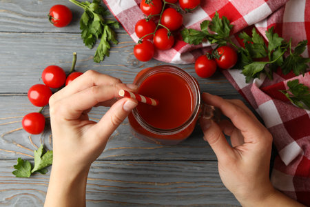 Female hands hold jar with tomato juice on wooden background with tomatoesの写真素材