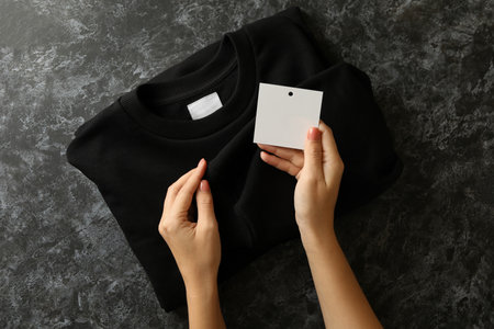 Female hands hold sweatshirt and blank tag on black tableの写真素材