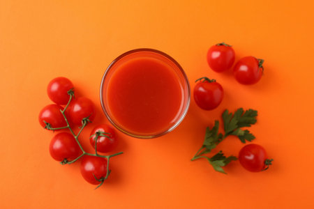 Glass of tomato juice and tomatoes on orange backgroundの写真素材