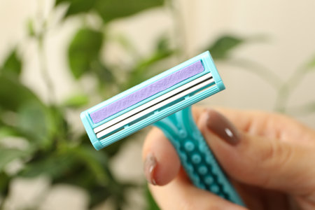 Female hand hold razor on blurred background, close up