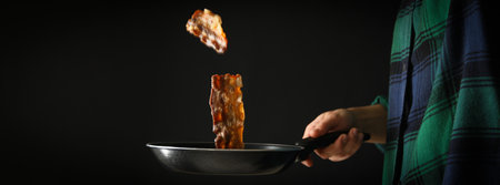 Woman fries bacon in a frying pan on a black backgroundの写真素材