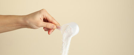 Female hand pouring washing powder on beige background