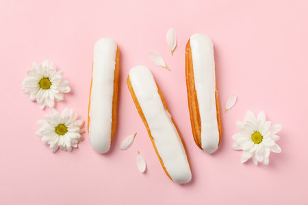 Delicious eclairs with custard and chamomiles on pink background