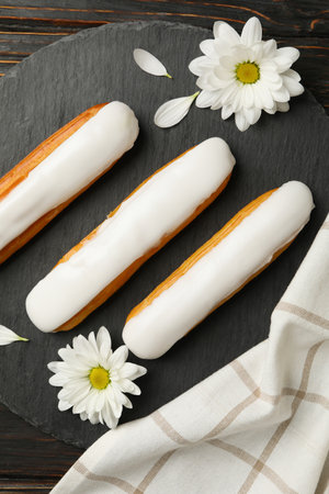 Tray with eclairs, chamomiles and towel on wooden background