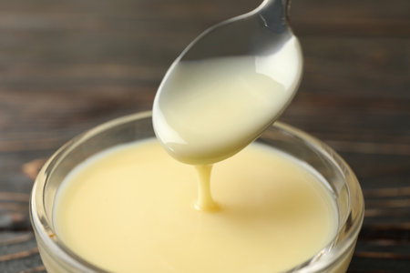 Spoon and bowl with condensed milk on wooden backgroundの写真素材