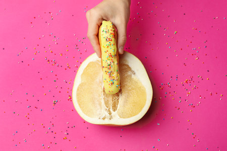 Female hand hold eclair on pomelo fruit on pink background with sprinkles