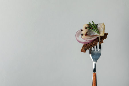 Fork with herring fish, bread and spices on light gray backgroundの写真素材