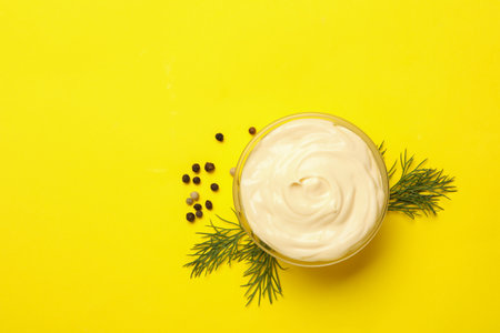 Bowl with mayonnaise, pepper and dill on yellow backgroundの写真素材