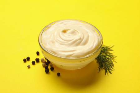 Bowl with mayonnaise, pepper and dill on yellow backgroundの写真素材