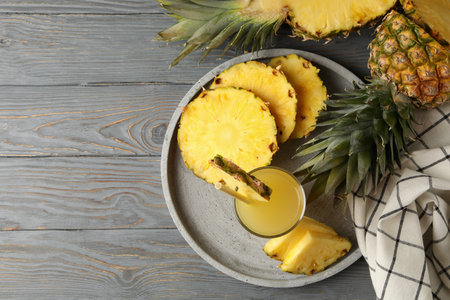 Tray with pineapple slices and glass of juice on wooden background, top view