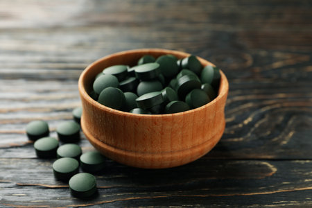 Wood bowl with spirulina pills on wooden background, close upの写真素材