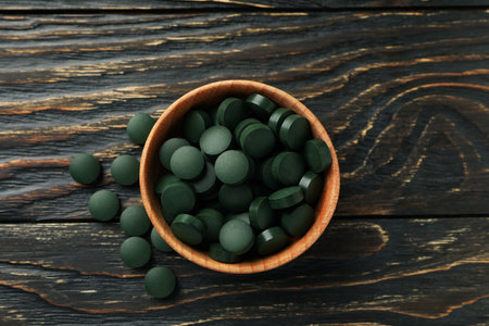 Wood bowl with spirulina pills on wooden background, top viewの写真素材