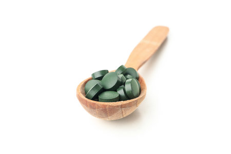 Wooden spoon with spirulina pills isolated on white backgroundの写真素材