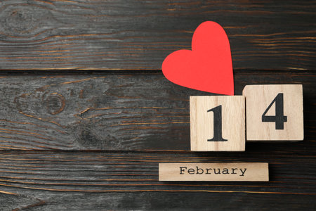 Wood calendar with 14 february and paper heart on wooden background