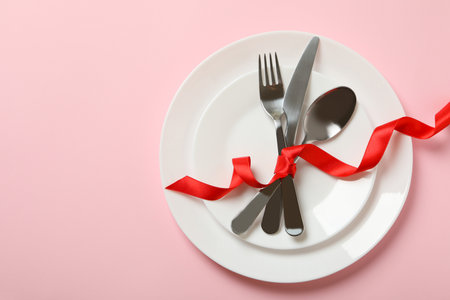 Plates with cutlery and red bow on pink backgroundの写真素材