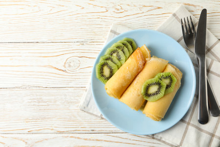 Concept of breakfast with plate of crepes rolls with kiwi slices on wooden tableの写真素材