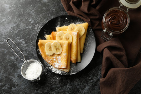 Concept of delicious breakfast with crepes with sugar powder and banana on black smokey backgroundの写真素材