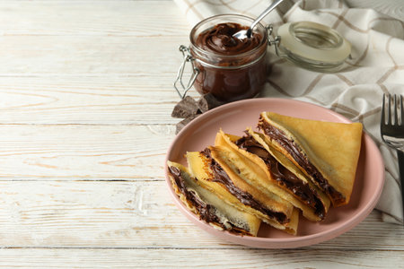 Concept of delicious breakfast with crepes with chocolate paste on white wooden backgroundの写真素材