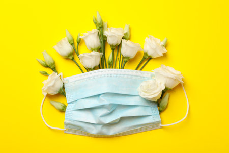 White roses and medical mask on yellow backgroundの写真素材