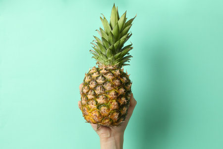 Female hand hold ripe pineapple on mint backgroundの写真素材
