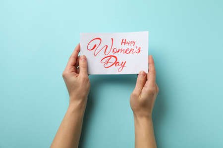 Female hands hold card with text Happy Women's Day on blue backgroundの写真素材