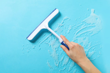 Female hand hold window cleaning squeegee on blue background with foam