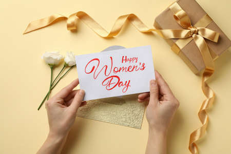 Female hands hold text Happy Women's Day on beige background with roses, envelope and gift box