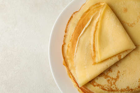 Plate with thin pancakes on white textured background