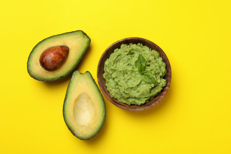 Bowl of guacamole and avocado on yellow background, top viewの写真素材