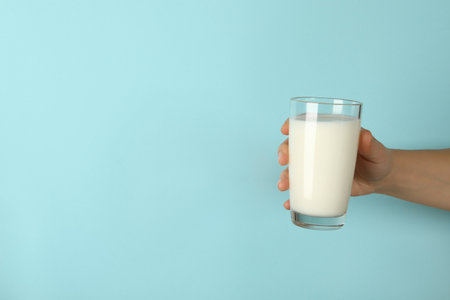 Female hand hold glass of milk on blue backgroundの写真素材