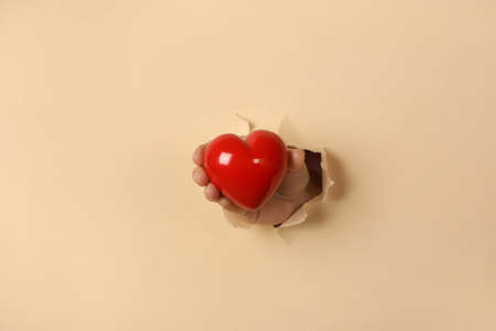 Female hand hold red heart through beige paper holeの写真素材
