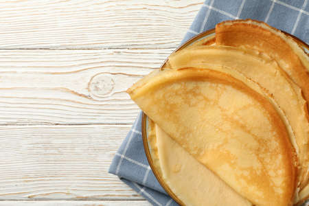 Kitchen towel with plate of thin pancakes on wooden background