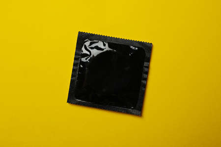 Black blank condom on yellow background, close upの写真素材