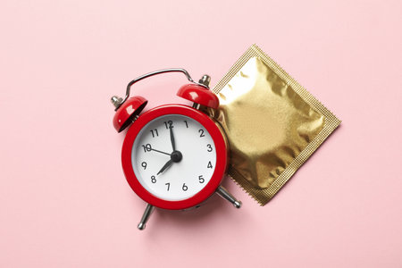 Alarm clock and condom on pink backgroundの写真素材