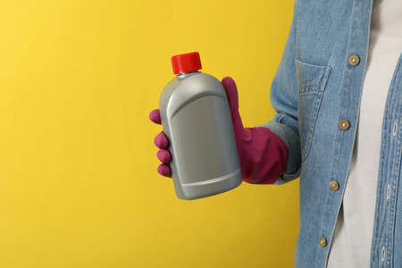 Woman in housework glove hold detergent on yellow backgroundの写真素材