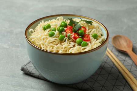 Concept of tasty eating with bowl of noodles on gray background