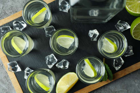 Board with bottle and shots of vodka with lime on gray backgroundの写真素材