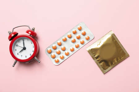 Alarm clock, condom and pills on pink backgroundの写真素材