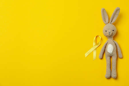 Toy bunny and child cancer awareness ribbon on yellow backgroundの写真素材