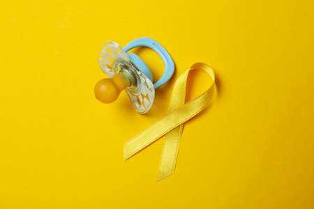 Pacifier and child cancer awareness ribbon on yellow backgroundの写真素材